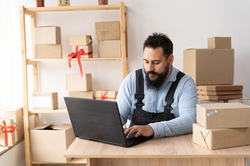 Small business aspiring entrepreneur, small and medium business freelance worker working in a home office man in overalls sits at a table and accepts an online order using an a laptop
