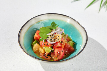 Vegetables salad with tomatoes, cucumbers and onion on white table with hard shadow. Vegan starter in asian style. Summer menu concept. Asian food in minimal design with sun light shadow.