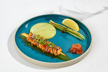 Squid yakitori in ceramic dish on white background. Japanese skewered squid with wasabi sauce. Grilled kalmar on bamboo skewer in asian style. Food menu for izakaya. Summer pan asian menu. © Ryzhkov