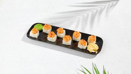 Maki sushi with salmon top on black plate. Sushi roll with philadelphia cheese inside and salmon tartare outside. Maki roll in minimal concept. Summer menu for japanese restaurant.