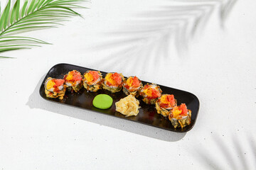 Tempura sushi roll with grapefruit and mango sauce. Hot maki sushi in black plate on white background. Summer menu for japanese restaurant. Modern sushi menu with hard shadow and leaves.