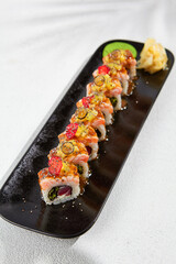 Modern asian food - maki sushi with salmon and berries on black plate on white concrete background. Sushi roll with tuna inside and salmon, mango and berries outside. Fusion sushi menu.