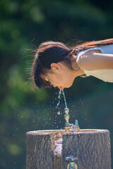 真夏の公園で水道水を飲んでいる可愛い小学生の女の子の姿