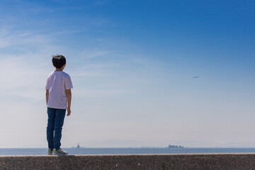 夏の海岸の堤防で立っている小学生の男の子の姿