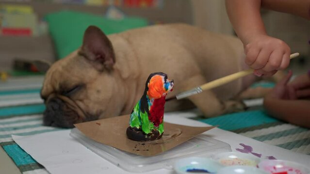 Little Child painting plaster dog statue next to sleeping dog at home.
