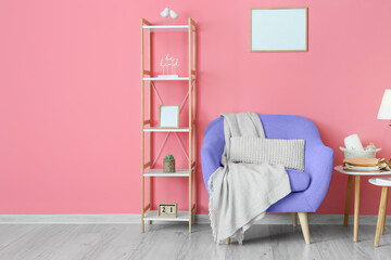 Interior of room with comfortable armchair and shelf unit near pink wall