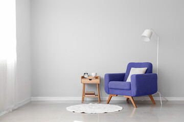 Stylish interior with table, lamp and armchair near light wall