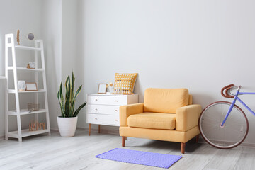 Stylish interior with bicycle, yellow armchair, chest of drawers and shelf unit
