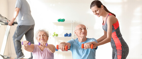 Young trainer helping elderly people to do exercises in gym