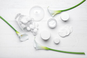 Composition with jars of cosmetic products, cotton balls, pads and calla lilies on light wooden background