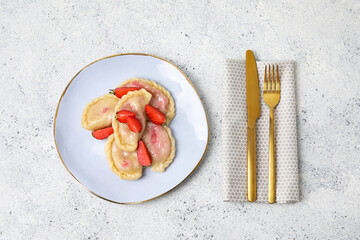 Plate with tasty strawberry dumplings and cutlery on light background
