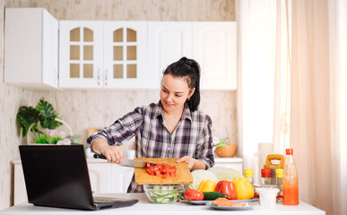 A cheerful young woman cooks in the kitchen with an online audience. The girl prepares a salad,...