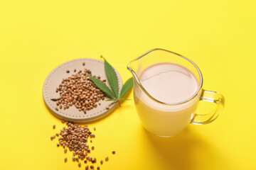 Pitcher of hemp milk and seeds on yellow background