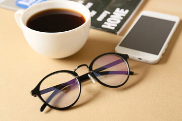 Eyeglasses, mobile phone, cup of coffee and magazine on beige background, closeup