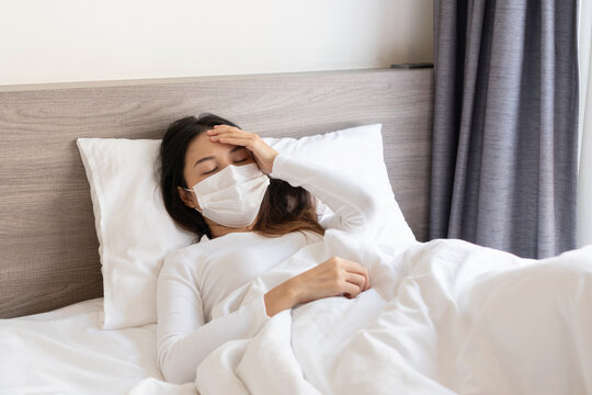 Young Asian woman wearing medical mask feeling sick with cold and fever at home. Ill girl
