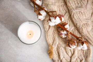 Holder with burning candle, cotton branch and sweater on table