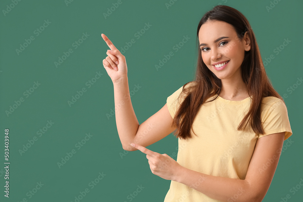 Sticker Pretty young woman in stylish t-shirt pointing at something on green background