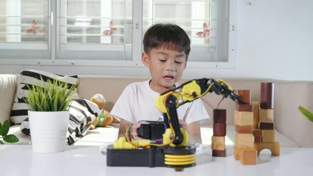 Happy Asian little kid boy using remote control playing robotic machine arm for pick up wood block, Funny child learning successful getting lesson control robot arm, Technology science education