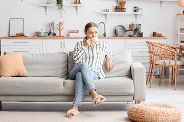 Young woman drinking tasty coffee on sofa in kitchen