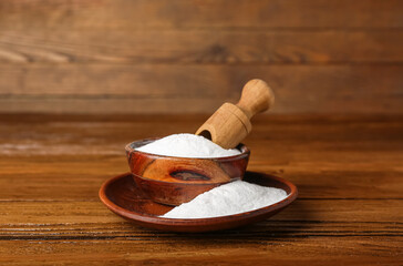 Bowl of baking soda and scoop on wooden background