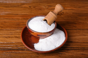 Bowl of baking soda and scoop on wooden background