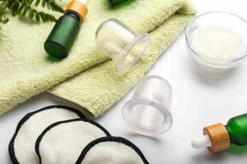 Vacuum jars for anti-cellulite massage, clean towel and bottles of essential oil on white background, closeup