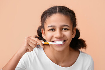 African-American teenage girl brushing teeth on beige background