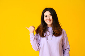 Inviting young Asian woman pointing at something on yellow background