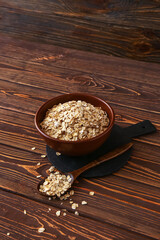 Bowl and spoon of raw oatmeal on wooden background