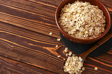 Bowl and spoon of raw oatmeal on wooden background, closeup