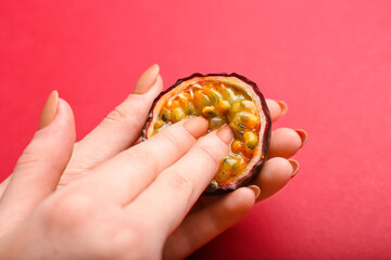 Female hands and half of passion fruit on red background. Erotic concept