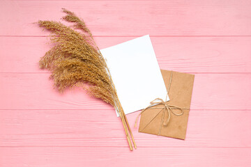 Envelope with blank card and pampas grass on pink wooden background