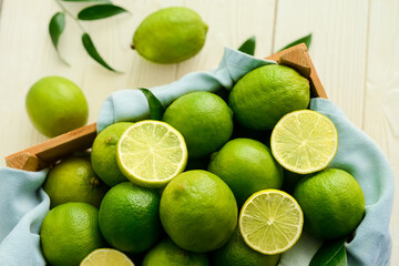 Box with fresh ripe limes on light wooden table, closeup