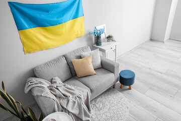 Interior of light living room with hanging Ukrainian flag, sofa and table