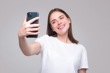 Fototapeta premium Happy young african woman casually dressed standing isolated over gray background, holding mobile phone. Girl making taking selfie.