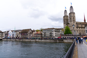 Old town of City of Zürich with protestant church Great Minster decorated with flags and River Limmat in the foreground on a rainy spring day. Photo taken April 24th, 2022, Zurich, Switzerland.