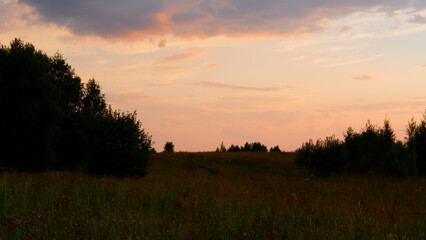 Rural landscape with field at sunset and village in the background. Vologda region