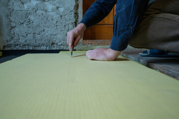 The master cuts expanded polystyrene on a floor, installation and warming of a floor in a room.