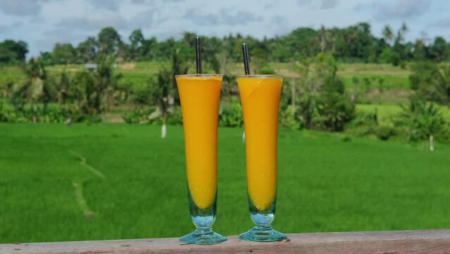 Fresh fruit juice on tropical background. In a glass glass with a thick bottom, a thick yellow soft drink is poured, which is pleasant to enjoy in hot weather. The drink is a natural fruit.