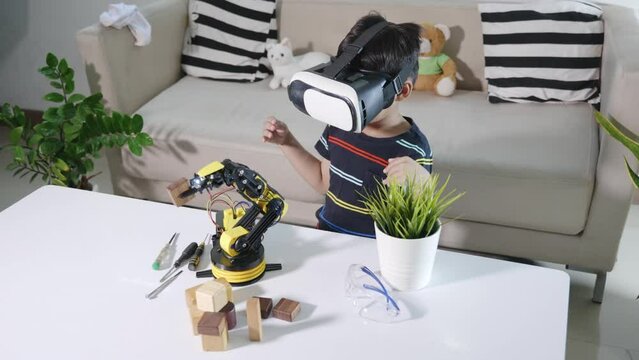 Asian kid boy using VR glasses on robotic arm in workshop, Child learning programer control robot arm with sensors to pick up wood block, Technology education, Virtual Reality Simulator, industry 4.0