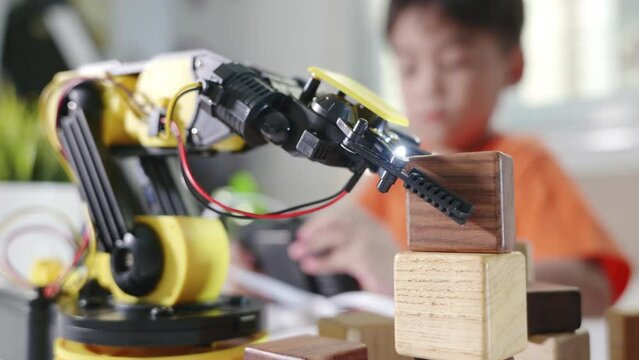 Happy Asian little kid boy using remote control playing robotic machine arm for pick up wood block, Funny child learning successful getting lesson control robot arm, Technology science education