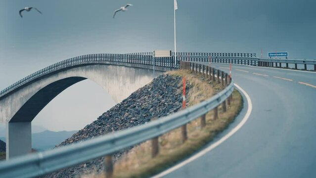Storseisundet bridge on the Atlantic road spanning above the turbulent waters. Seagulls fly low above the road. Slow-motion, pan forward.