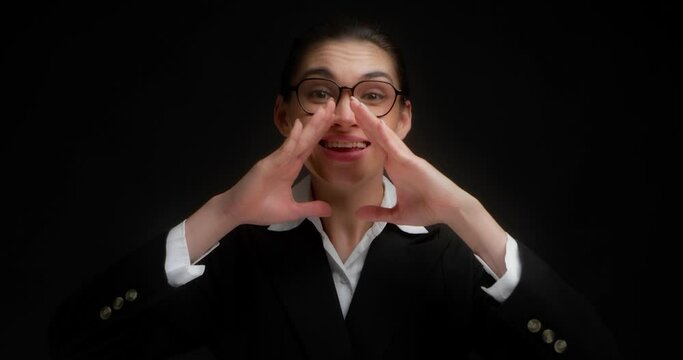 Business woman in glasses and office clothes is looking for you,presses her hands to her mouth,screams loudly.Asian woman wants to share important information.Hey, where are you.On a black background