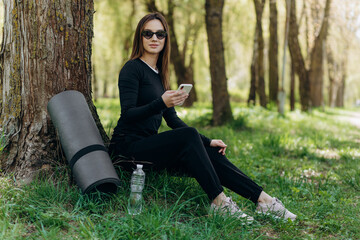 Young attractive fit caucasian sportswoman standing in nature and using smart phone to search music...