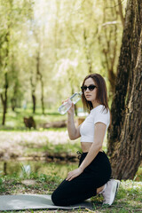 Close view of woman with dark hair drinking water from plastic bottle outdoors after intensive training