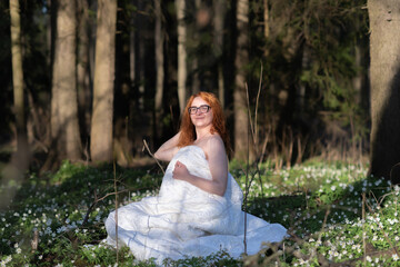 Portrait of a young beautiful red-haired girl wrapped in a white blanket in the forest.