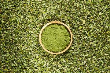 A wooden bowl filled with moringa powder, surrounded by moringa leaves