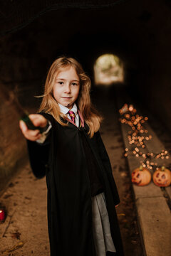 Girl with magic wand wearing witch costume standing in spooky tunnel