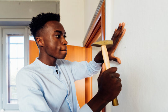 Young man using hammer on wall at home