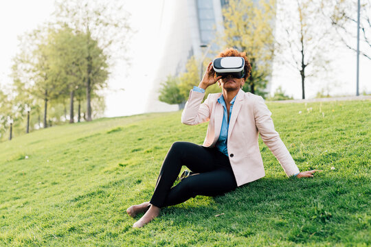 Businesswoman wearing virtual reality simulator sitting on grass